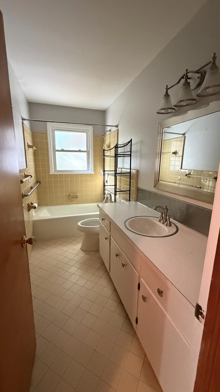 Bathroom before renovation, with yellow tile around the tub and a single-sink vanity