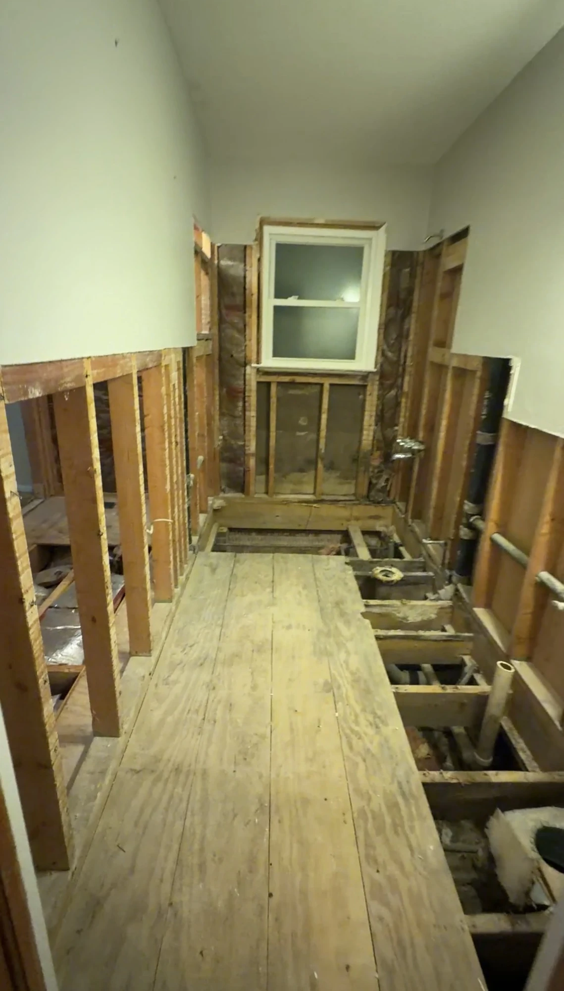 Bathroom during demolition with wall framing and sections of the floor exposed