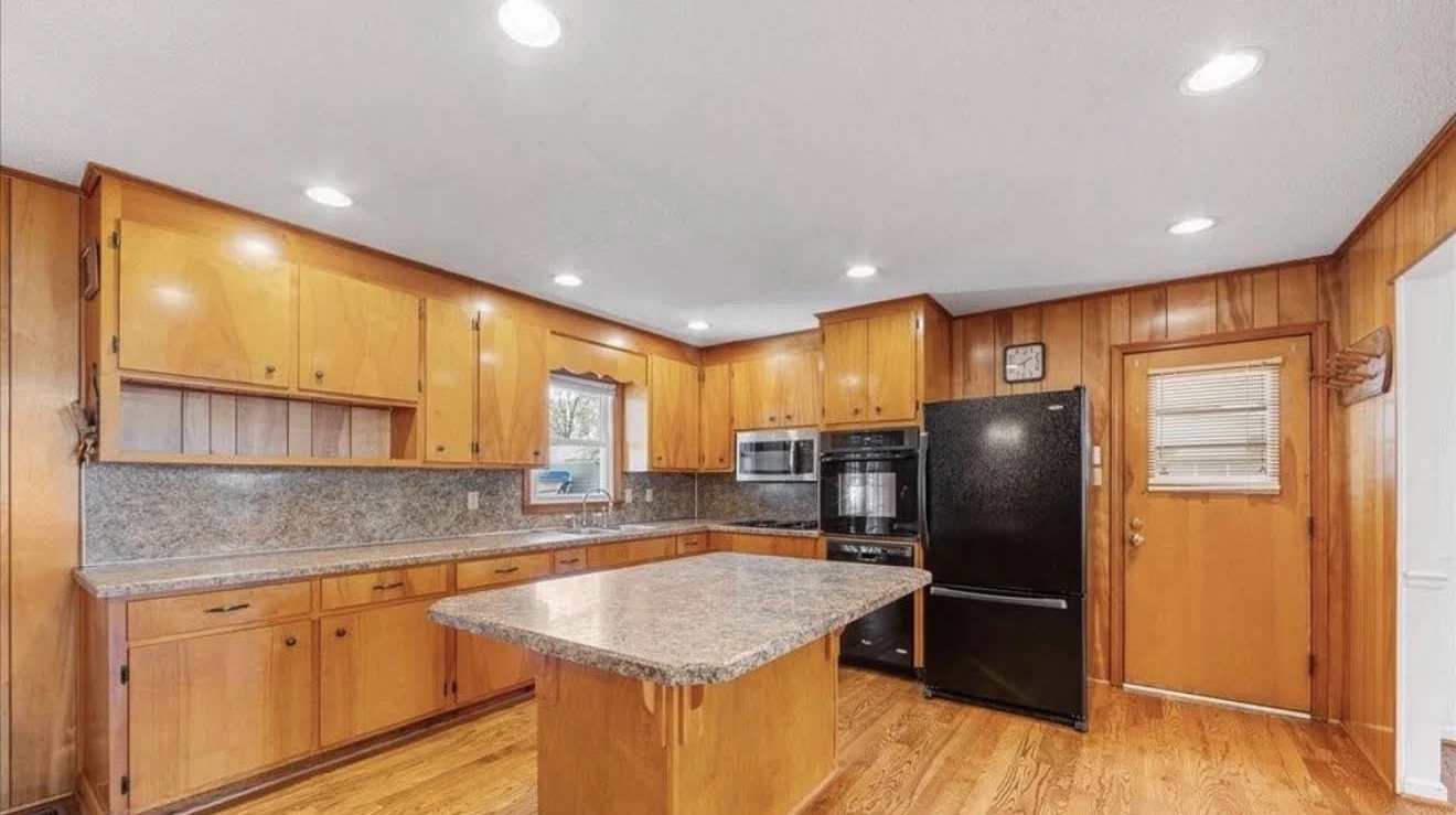 Kitchen before renovation with wood cabinets, paneled walls and a central island